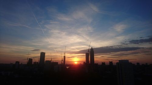 Silhouette of city against cloudy sky during sunset