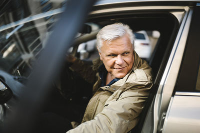 Smiling senior businessman opening door while disembarking from car