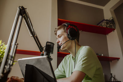 Smiling teenage boy podcasting near laptop at home