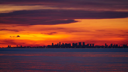 Silhouette of buildings against cloudy sky during sunset