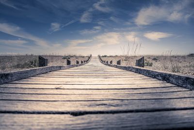 Surface level of boardwalk on field against sky