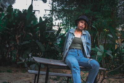 Smiling young woman sitting on seat against trees