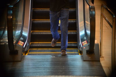 Low section of man walking opposite escalator