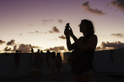 Silhouette people photographing on beach during sunset