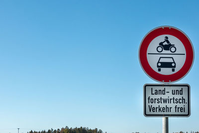 Low angle view of road sign against clear blue sky