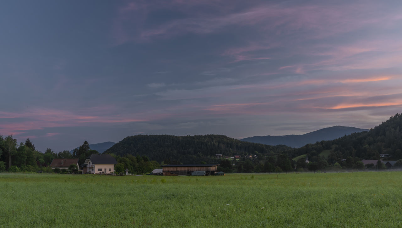 HOUSES ON FIELD AGAINST SKY DURING SUNSET