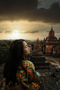 Woman looking at temple against sky during sunset