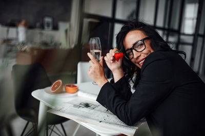 Portrait of woman holding champagne flute and strawberry at restaurant