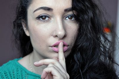 Close-up portrait of young woman with finger on lips