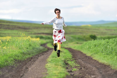 Joyful young woman in skirt running in canola field in the spring