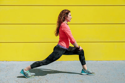 Full length of woman looking away against yellow wall