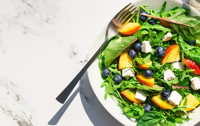 Salad with nectarines, blueberries, arugula, spinach and feta cheese on white marble background