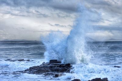 Waves splashing on rocks against sky