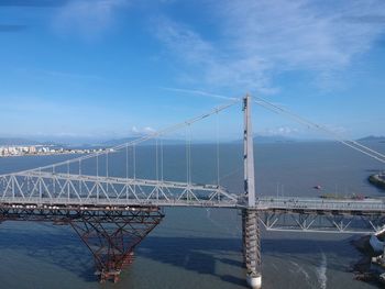 Suspension bridge over sea against cloudy sky