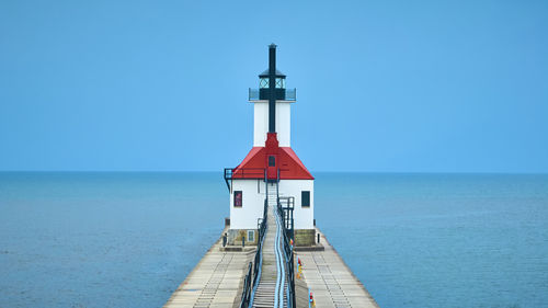 Lighthouse by sea against clear blue sky