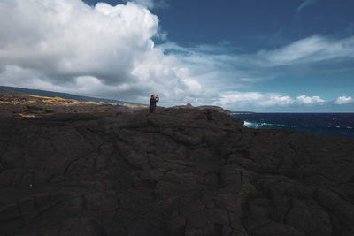 Man standing on rock by sea against sky