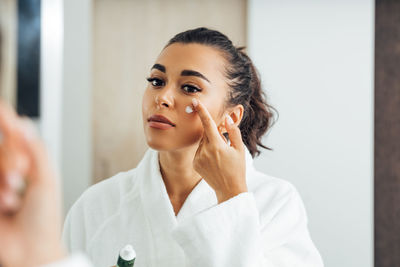 Beautiful woman applying moisturizer on face