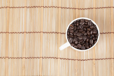 Roasted coffee beans in cup on place mat