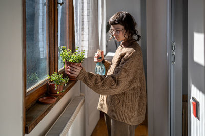 Caring teen girl pouring spraying water watering potted flower, enjoying growing cultivating plants