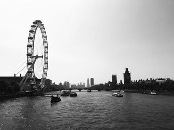 Ferris wheel by river against sky in city