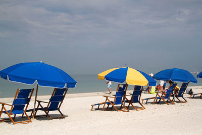 Blue wooden sun chairs with umbrellas on sandy seashore