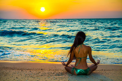 Rear view of woman sitting on beach during sunset