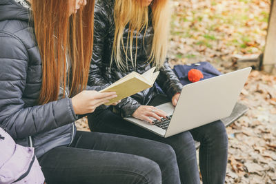 Girls study sitting on a bench in the park. teens students using laptop and reading a book outdoor. 