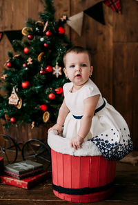 Portrait of cute baby girl in basket with christmas tree at home