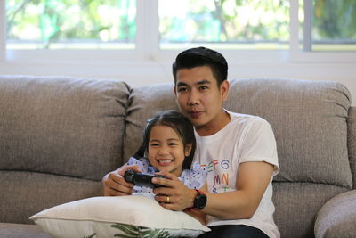 Father and daughter playing video game while holding remote control on sofa