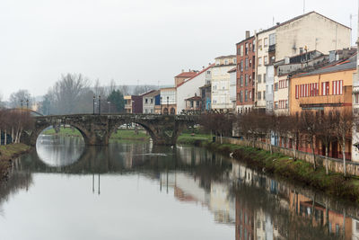 In orense, spain, a picturesque bridge spans a calm river surrounded by trees