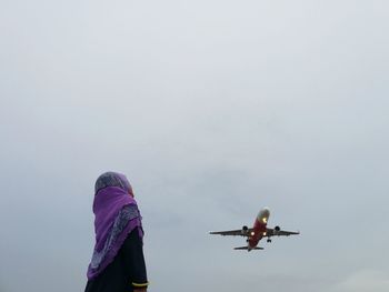 Girl in traditional clothing looking at airplane flying against sky