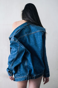 Rear view of woman wearing denim jacket standing against white wall