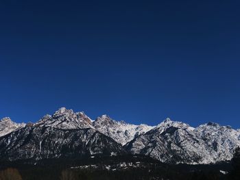 Low angle view of snowcapped mountains against clear blue sky