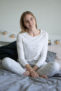 Portrait of smiling young woman sitting on bed at home