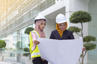 Female architects examining blueprint while standing outside office building