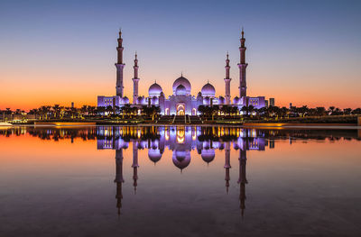 Reflection of illuminated buildings in lake against sky during sunset