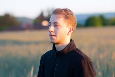 Portrait of young man looking away while standing on field