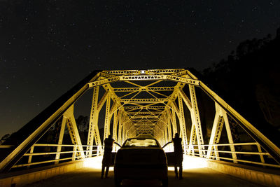 Silhouette people standing by car on bridge against sky at night