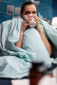 Portrait of young woman drinking from while sitting on bed