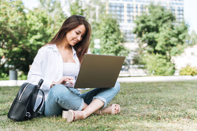 Young asian woman student freelancer with long hair working on laptop in city park