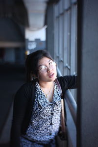 Woman looking away while standing against wall