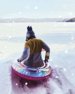Rear view of young woman sitting on inflatable ring on frozen sea