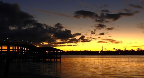 Silhouette bridge over river against sky during sunset