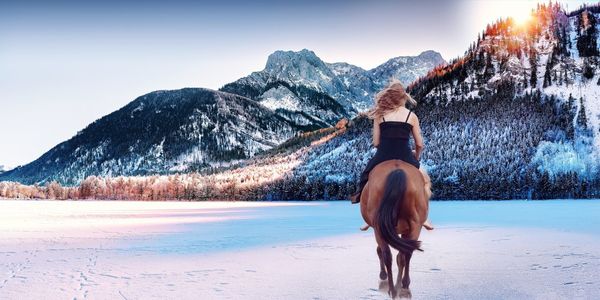 Rear view of woman riding horse on snow covered landscape against clear sky