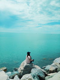 Rear view of woman sitting on rock by sea