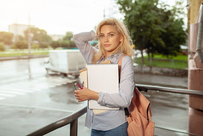 Portrait of a beautiful young woman standing against railing