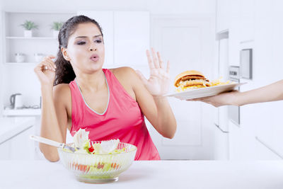 Woman with salad bowl denying burger at home