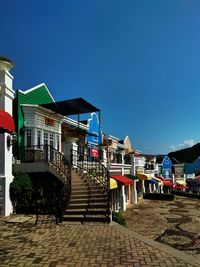 Footpath amidst buildings against clear blue sky