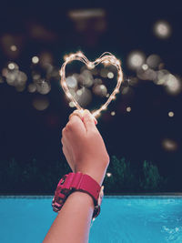 Cropped image of woman holding illuminated light in front of swimming pool at night