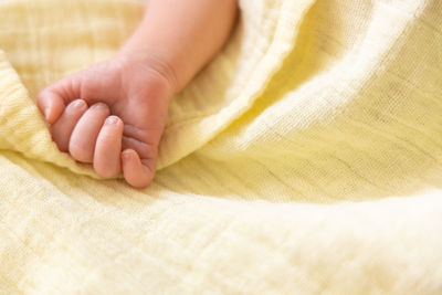 Newborn caucasian premature baby hand on pastel yellow soft muslin blanket. copy space, space for